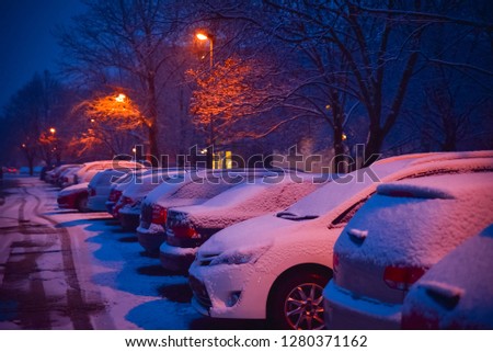Cars parks in the winter evening city. Snow on the roof