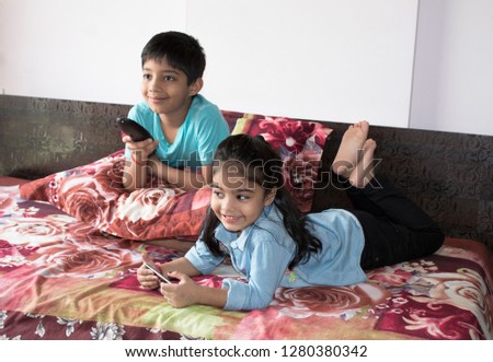 Girl using mobile phone while brother is watching tv on bed Royalty-Free Stock Photo #1280380342