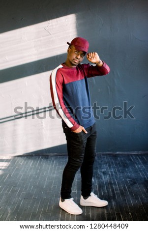 stylish Afro guyPortrait of an African-American hipster guy dressed in a red fleece sweater and red cap at the studio. Isolated on dark textured background student wearing sportswear