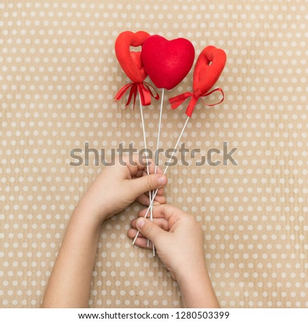 Valentines day. The child is holding red hearts on sticks against the background of cardboard paper in white peas.. Valentine Day. Heart pendant. Space for text. Red heart. Eighth of March.