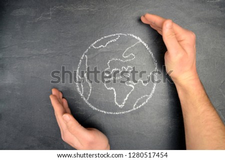 On a dark stone surface, a globe was painted and a person holds her hands protectively around the globe - concept to save the earth from driven and threats