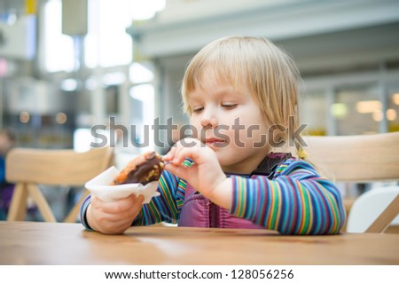 Adorable girl eat chocolate donut in fast food restaurant in mall