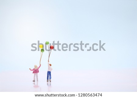 Miniature couple holding balloons on blue background with copy space. Love and valentine's day concept