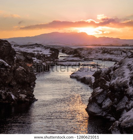 River flowing into the distance with the sun setting over mountains in the background