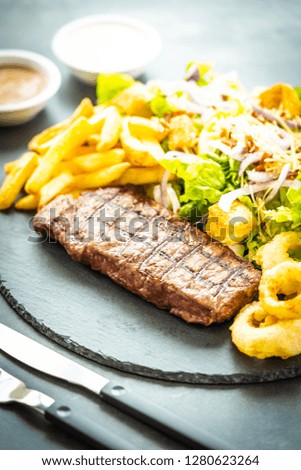Grilled beef meat steak with french fries onion ring with sauce and fresh vegetable in black slate
