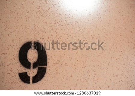 A close up on black stenciled number nine on orange wall