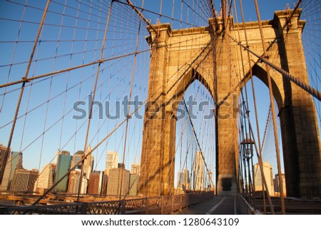 Arch of Brooklyn bridge and cables in front of skyscrapers of Manhattan with blue sky
