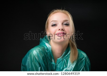 Portrait of a young blonde woman in a green raincoat looking at the camera. Shooting in a photo studio on a black background