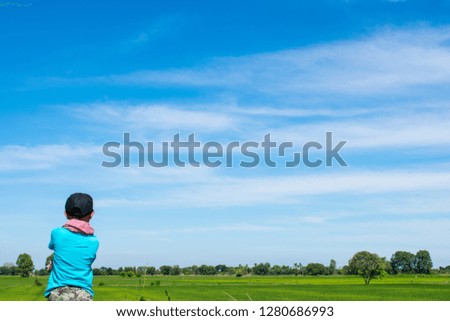 Holiday concept, A child boy with camera taking pictures at the side road on summer day among green trees and light sky background.