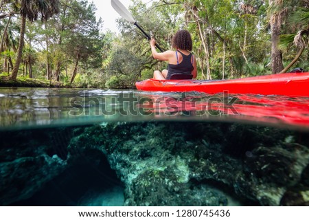 Over and Under picture of a girl kayaking in a lake near an underwater cave formation. Taken in 7 Sisters Springs, Chassahowitzka River, Florida, United States of America.