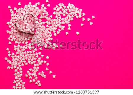 Love and marriage concept. Valentine's Day. Two golden wedding rings lying in a metal heart among lots of light pink small hearts on a pink background with a copy space.