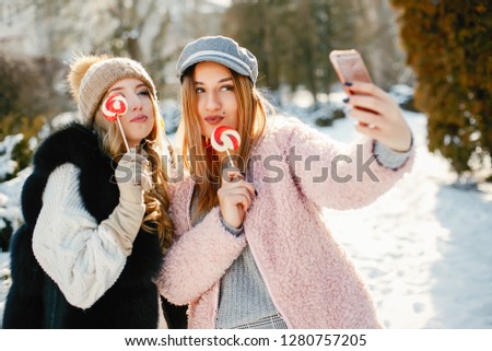 Two young and stylish girls in the winter clothes are walking in the solar park with candyes
