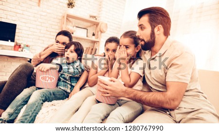 Cheerful Family Watching Scary Movie at Home. Kids Eating Popcorn and Smiling while Sitting on Couch at Home. Small Cute Kids are with Toys, Parents are on the Sofa, Hugging, Watching Cartoons