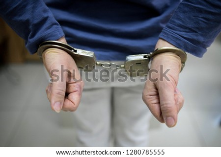 Close-up. Arrested man handcuffed hands at the back isolated on gray background. Prisoner or arrested terrorist, close-up of hands in handcuffs.