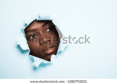 Young afro american woman with make up face skincare inside hole on blue background