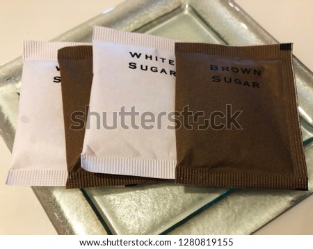 sugar in paper packages on a glass plate. white sugar and brown sugar to cater to customer preference.