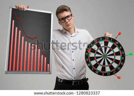 Young man in glasses holding a Board with falling statistics and Darts isolated on white background