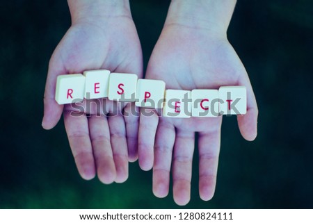 Hands holding the word of respect, as a base of all of the relations of human beings, no matter, religion, ideology or nationality. Dark black and green background. Text, flat lay, top view.