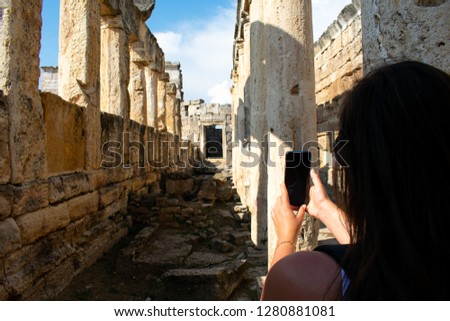 Rear view of woman taking picture of Old ancient ruins of roman City Hierapolis in Pamukkale, Turkey 