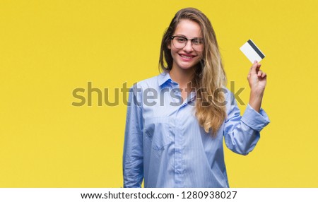 Young beautiful blonde woman holding credit card over isolated background with a happy face standing and smiling with a confident smile showing teeth