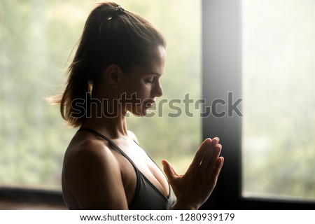 Portrait of young calm sporty woman practicing yoga pose, doing meditating exercise, Namaste mudra gesture, working out, wearing sportswear, indoor close up, yoga studio. Mindful healthy life concept