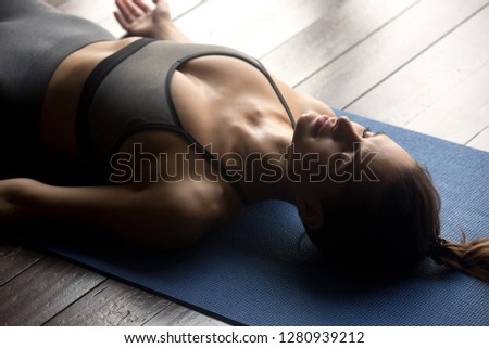 Young sporty woman practicing yoga, doing Dead Body, Savasana exercise, Corpse pose, working out, wearing sportswear, grey pants and top, indoor close up, yoga studio Royalty-Free Stock Photo #1280939212