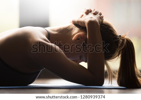 Young woman practicing yoga, supporting neck muscle groups, pose to muscle group against neck injuries, working out, wearing sportswear, indoor close up view, yoga studio