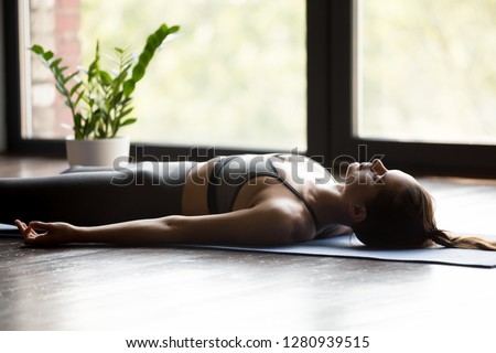 Young sporty woman practicing yoga, doing Dead Body, Savasana exercise, Corpse pose, working out, wearing sportswear, grey pants and top, indoor close up, yoga studio Royalty-Free Stock Photo #1280939515