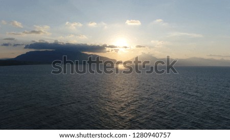 Aerial birds eye photo of coastal ocean landscape showing quiet water below and mountains in background sunshine through low hanging clouds shot early evening
