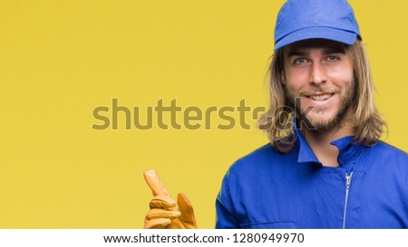 Young handsome mechanic man with long hair over isolated background with a big smile on face, pointing with hand and finger to the side looking at the camera.