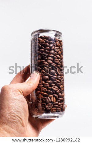 Plastic transparent bottle with coffee grains on a white background in hand