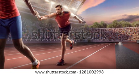 Male athletes sprinting. Runner passes the baton at the running track in professional stadium Royalty-Free Stock Photo #1281002998