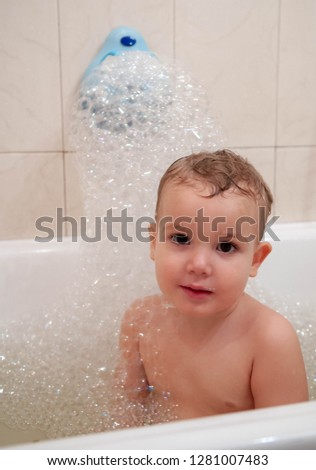 Cute baby takes a bubble bath, looks into the frame and smiles. Handsome boy in the bath with foam.