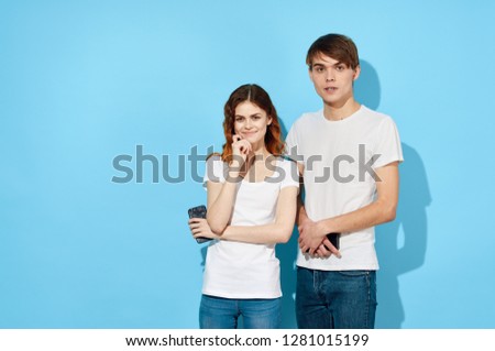 A young couple in white T-shirts is standing next to the phones in their hands on a blue background                