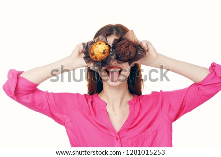 A woman in a pink shirt holds cupcakes near her eyes              