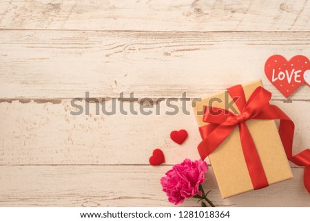 Kraft gift box with red ribbon bow and carnation, concept of giving present at mother's day as surprise, flat lay, top view