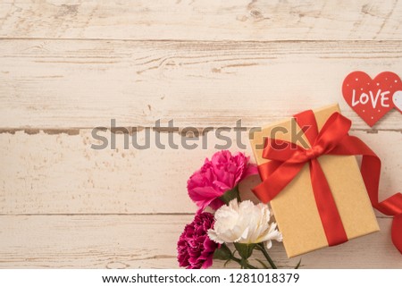 Kraft gift box with red ribbon bow and carnation, concept of giving present at mother's day as surprise, flat lay, top view