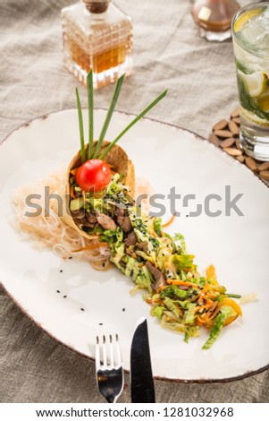salad with beef, sesame seeds and vegetables in tortilla on white plate studio shot