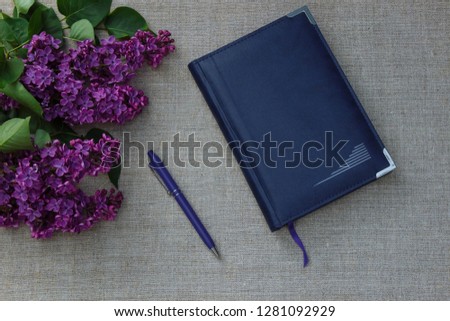 notebook with blue cover and handle on linen tablecloth and lilac bouquet top view
