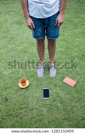 Man with smartphone, cup of coffee / tea and notebook on a grass.