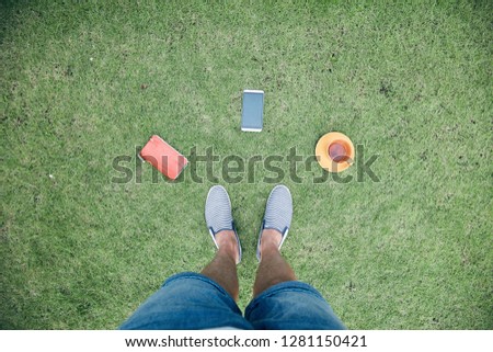 Man with smartphone, cup of coffee / tea and notebook on grass.