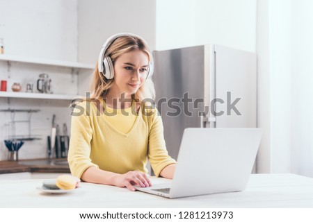 attractive blonde woman listening music in headphones while using laptop Royalty-Free Stock Photo #1281213973