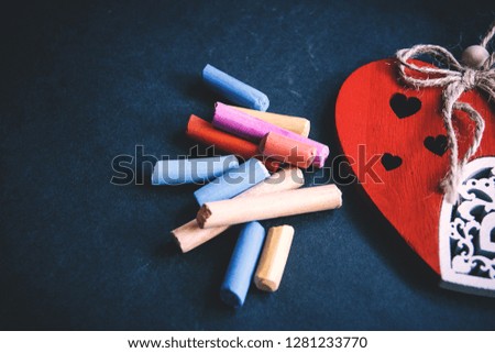 handmade red heart close-up and pieces of pastel chalks on dark background, symbol of love, happy Valentine's day.