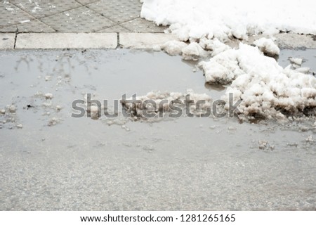 Sidewalk with crosswalk covered with melted snow and water pot hole in the winter 