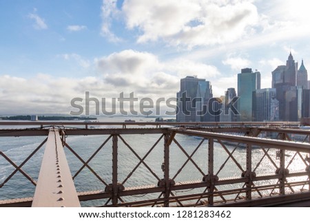 Behind the steel structures of the Brooklyn Bridge you can see the skyscrapers of Manhattan and in the distance the Statue of Liberty in New York, United States