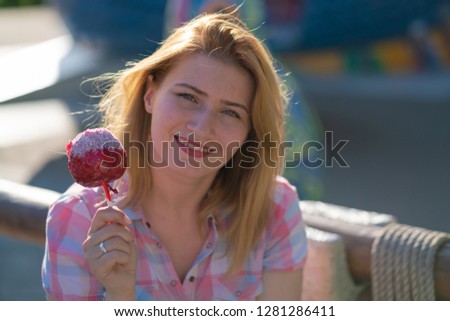 cute emotional caucasian girl eats red apple in caramel in the park in sunny bright day