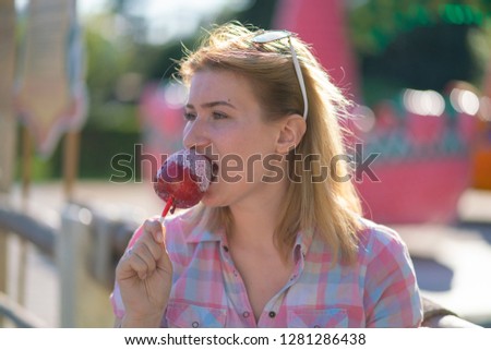 cute emotional caucasian girl eats red apple in caramel in the park in sunny bright day