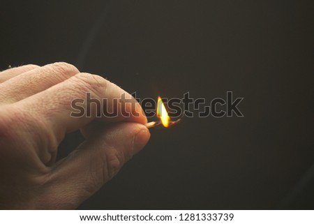  Burning wooden match in hand on dark background                              