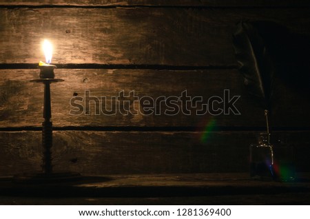 Quill pen in a inkpot and burning candle on the writer desk table background with copy space. Education concept.