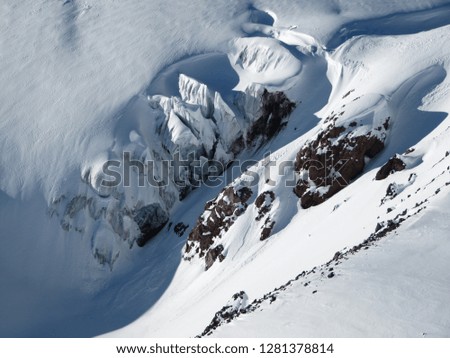 Top view of the glacier and snow-capped mountains and protruding rocky cliffs on a Sunny day